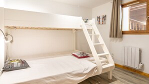 Un lit superposé avec une échelle, une table de chevet, un radiateur fixé au mur et une fenêtre avec des rideaux.