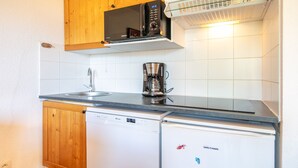 Une cuisine compacte équipée d’un four à micro-ondes, d’une machine à café, d’un lave-vaisselle et de meubles de rangement en bois.