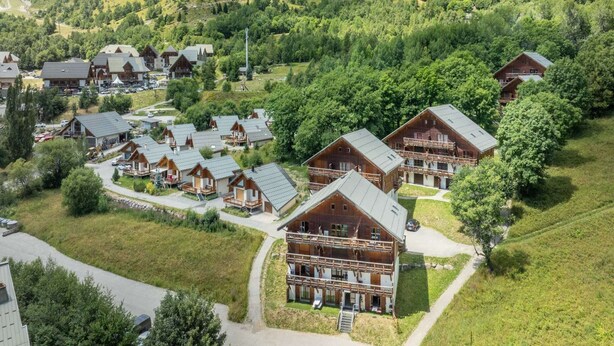 A cluster of wooden cabins with sloped roofs, surrounded by lush greenery and hills. - Mountain Apartment in Saint-Sorlin (Saint-Sorlin-d´Arves)