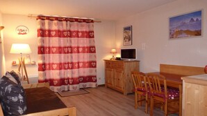 A cozy room with a bed, a desk with a computer, a dining table with chairs, and a TV. - Mountain Apartment in Saint-Sorlin (Saint-Sorlin-d´Arves)