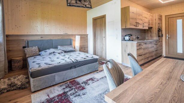 Een houten interieur met een bed, een eettafel en een keukenhoek.