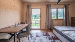 Une pièce de style cabane en bois, comprenant un lit, une table avec des chaises, une fenêtre avec des rideaux et une vue sur l’extérieur.
