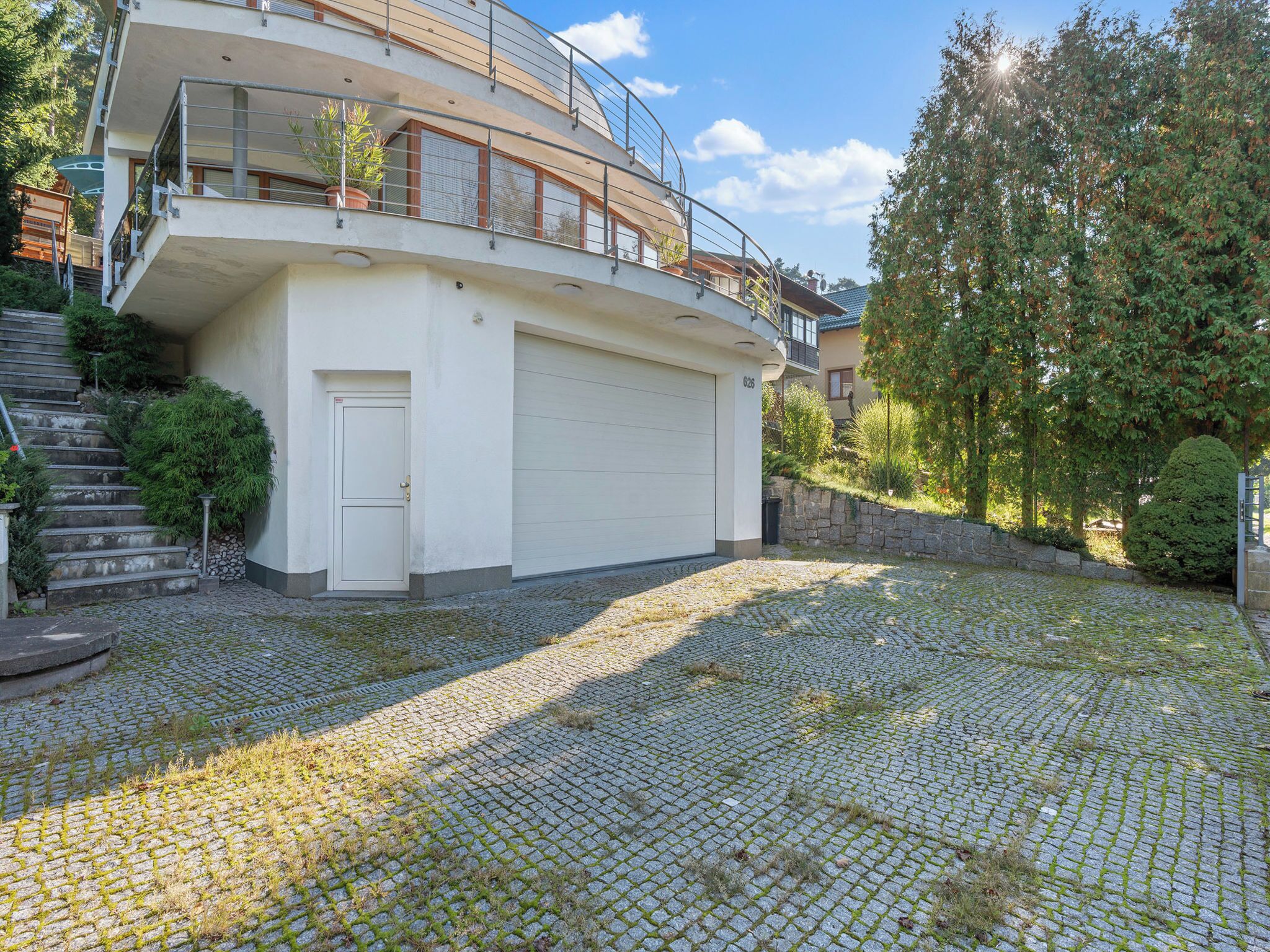Ein modernes, zweistöckiges Haus mit Garage, Kopfsteinpflasterauffahrt und einer Treppe, die zum Eingang führt.