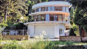 A multi-level, modern building with balconies, surrounded by dense forest.