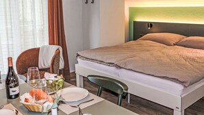 A hotel room with a neatly made bed, a dining table with a bottle of wine, glasses, and a basket of bread. - Juliana by Interhome (Zermatt)