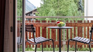 A balcony with a wooden fence, two chairs, and a table with a fruit bowl. - Juliana by Interhome (Zermatt)