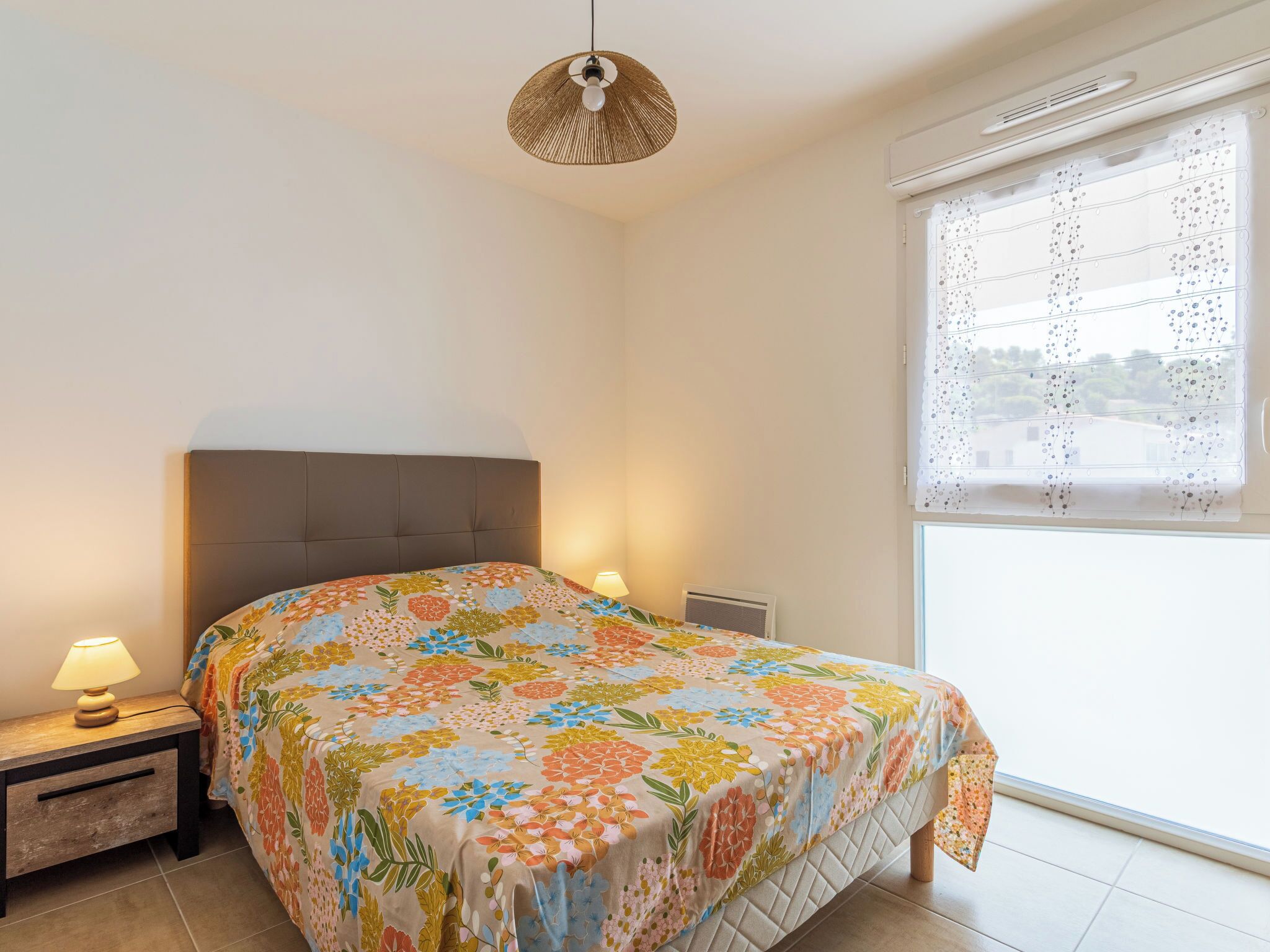 A bedroom with a bed, two bedside lamps, a window with curtains, and a ceiling fan.