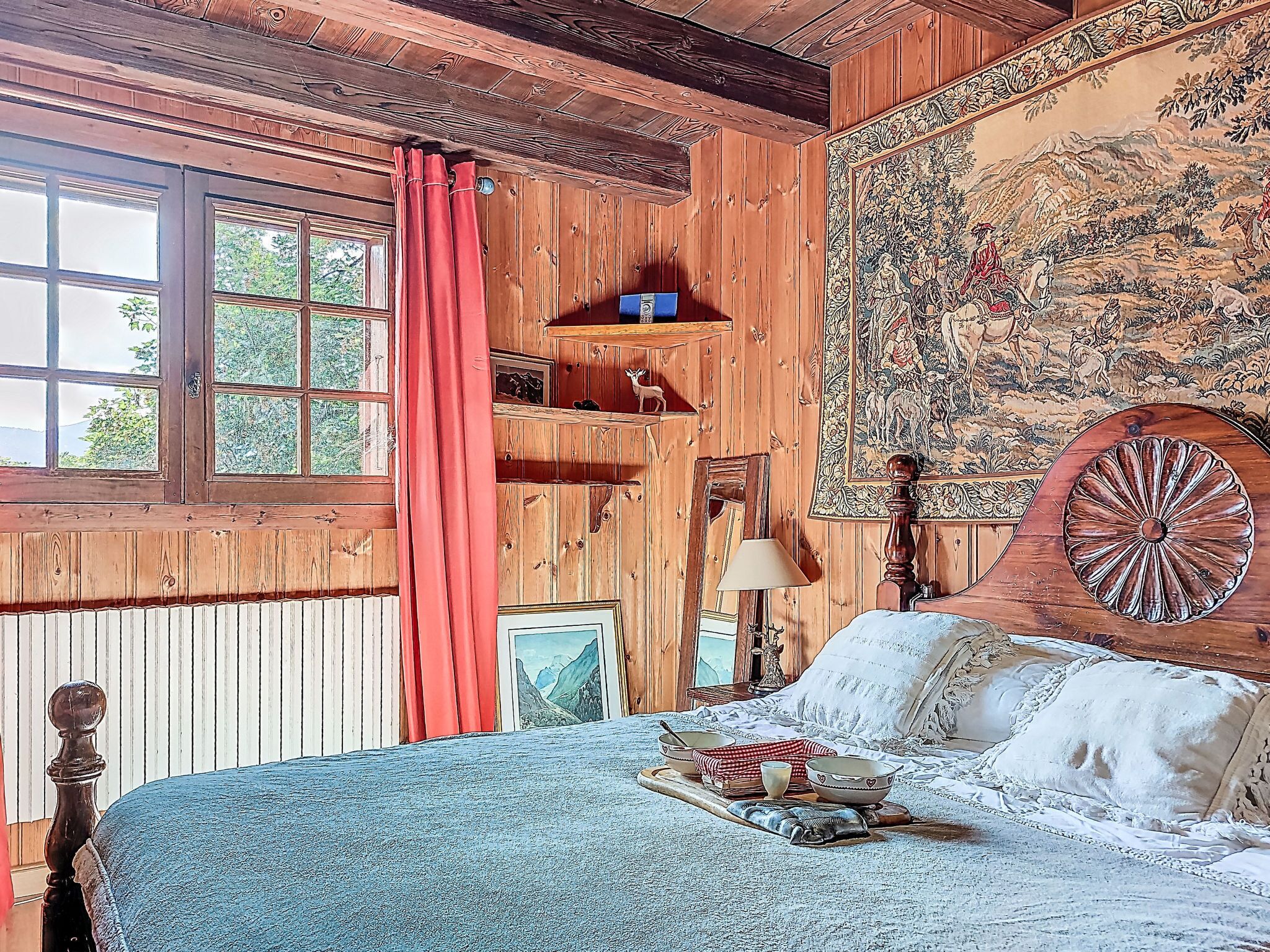 Une pièce de style cabane en bois, avec un lit, une fenêtre ornée de rideaux rouges, une tapisserie et un plafond en bois.