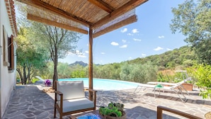 A covered outdoor area with a pool, stone flooring, and wooden furniture.