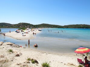 Una playa con aguas transparentes, orilla de arena y algunas sombrillas.