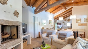 A cozy living room with a stone fireplace, wicker furniture, and a wooden ceiling.