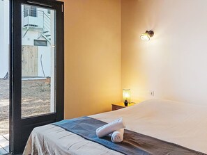 Et hotelværelse med en seng, et natbord med lampe, et vindue med udsigt, og en vægmonteret lampe.