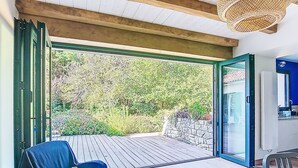 Una habitació amb terrassa de fusta, una cadira blava i una paret de pedra.