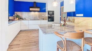 Cuina moderna amb parets d'accent blaves, una illa central i una zona menjador amb cadires de fusta.