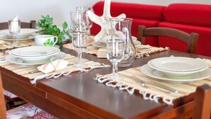 A dining table set with plates, glasses, and a pitcher, with a red couch and floral artwork in the background.