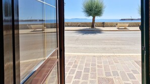 Vista desde una habitación con puerta de vidrio que da a un espacio exterior con pared de piedra, una banca y un árbol.