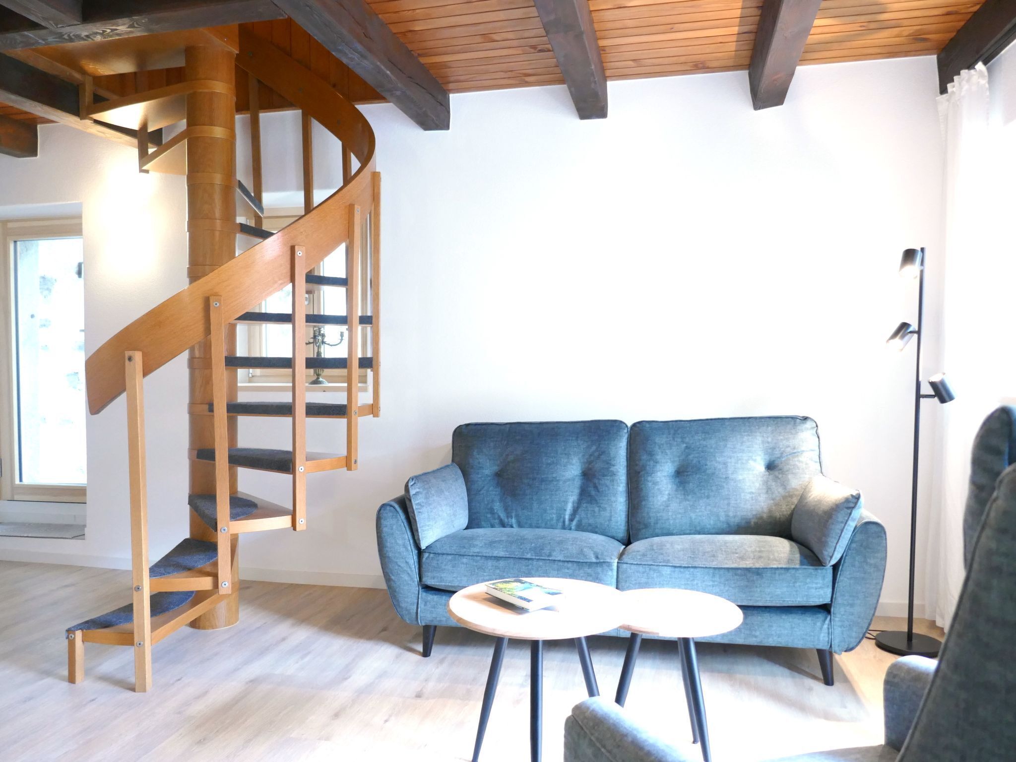 Un soggiorno con una scala a chiocciola in legno, un divano blu e un piccolo tavolino rotondo.