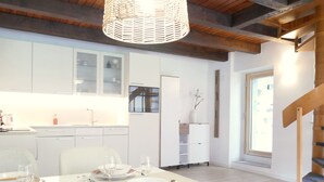 A modern kitchen with white cabinets, a dining area with a table set for four, and a wooden staircase. - Rustico Emilio by Interhome (Roveredo)