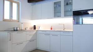 A modern kitchen with white cabinets, a built-in oven, and a window above the sink. - Rustico Emilio by Interhome (Roveredo)
