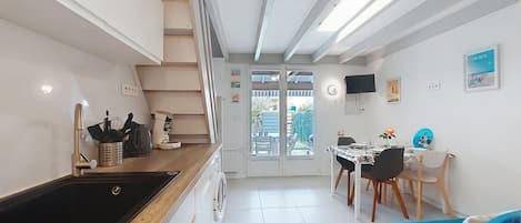 Uma cozinha moderna com forno embutido, máquina de café e pia. Há uma área de jantar com mesa e cadeiras, e um sofá azul.