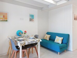 Ein Essbereich mit einem Tisch, gedeckt für vier Personen, einer blauen Couch mit gemusterten Kissen und zwei gerahmten Bildern an der Wand.