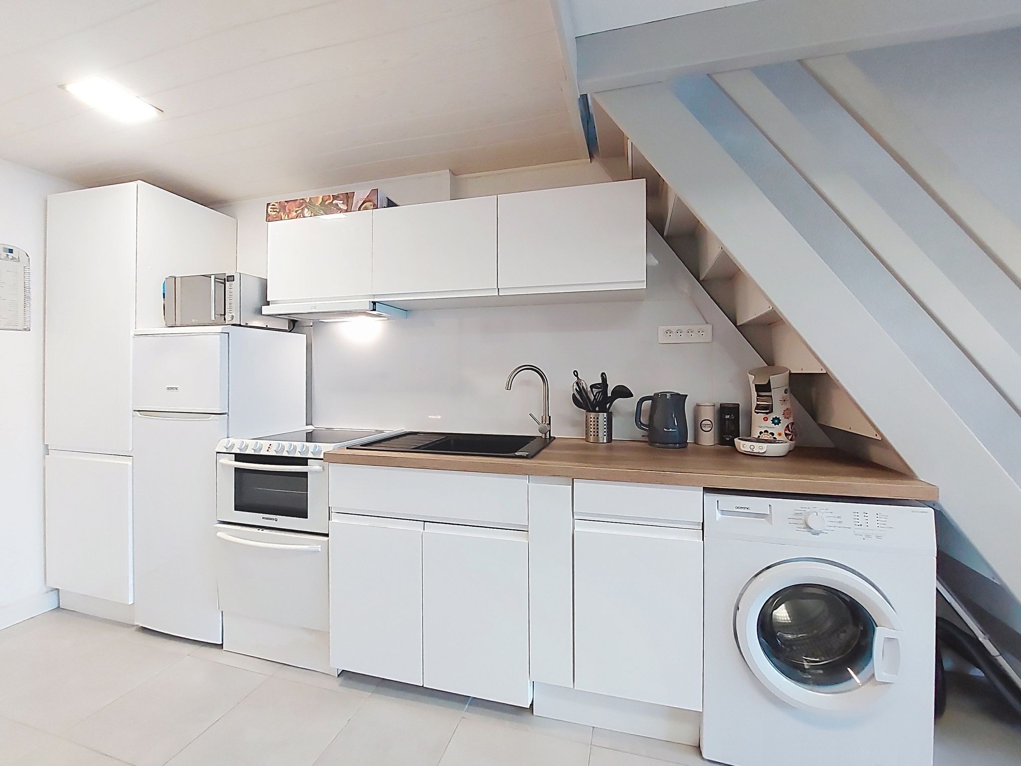 Une cuisine compacte avec des meubles blancs, un four encastré, un four à micro-ondes, un évier et un lave-linge.