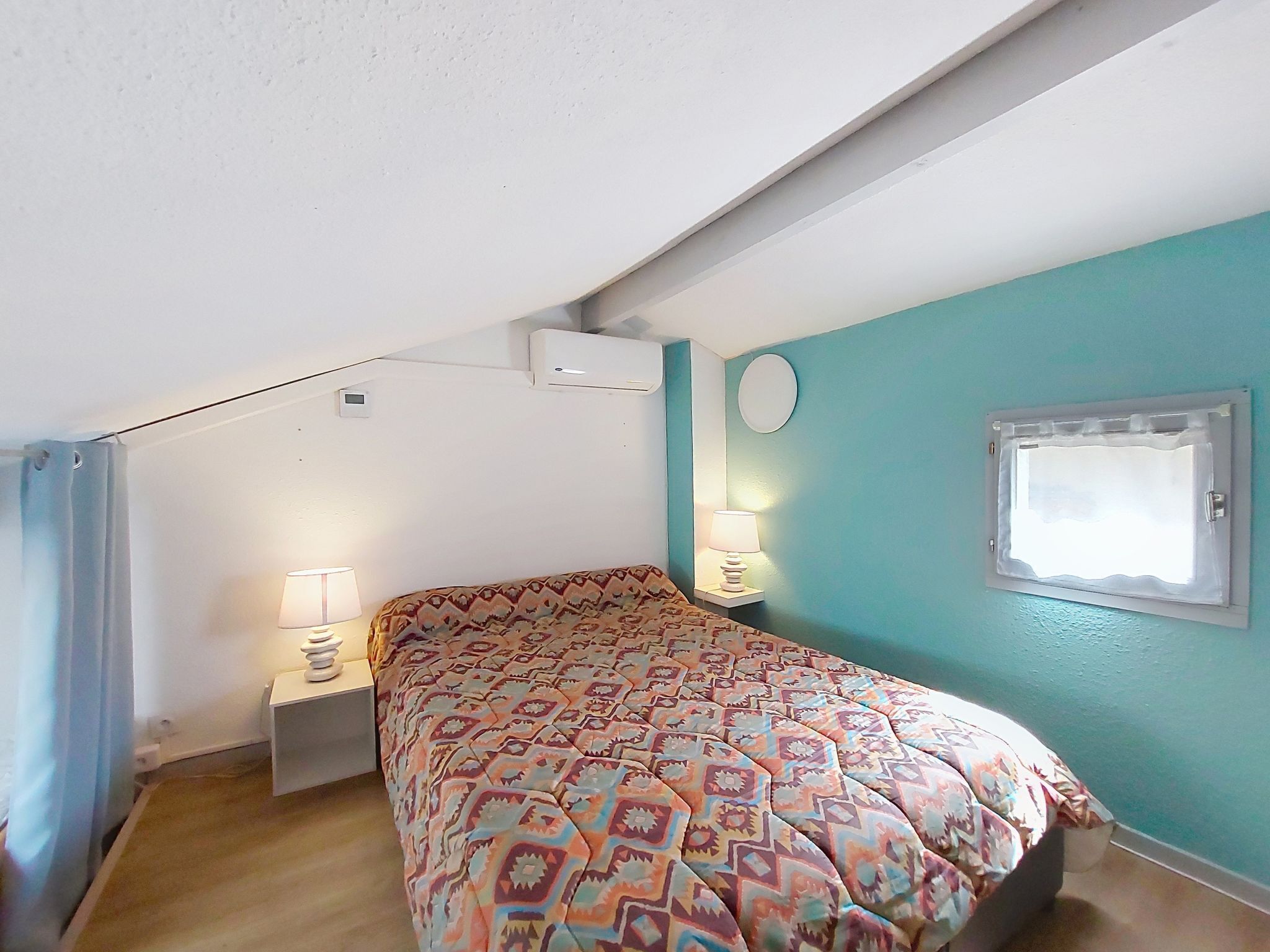Een slaapkamer met een bed met een decoratieve spreidek, een raam met uitzicht en een plafondventilator.