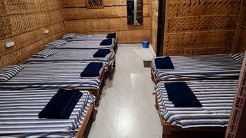 A room with four wooden beds, each with striped bedding and dark pillows. The room has a tiled floor and a small window with a grid pattern.