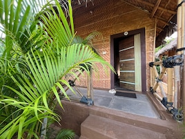 A rustic building with a wooden door, a thatched roof, and a palm tree in the foreground.