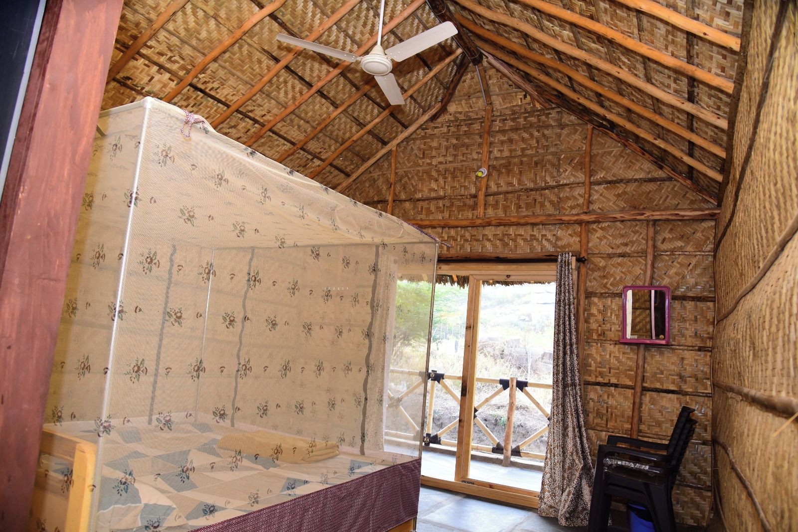 Quarto com cama, ventilador de teto, janela com vista e uma pequena mesa.