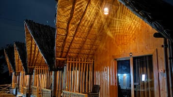 A row of wooden cabins with thatched roofs, each featuring a balcony and a small porch area.