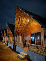 A row of wooden cabins with thatched roofs, each featuring a balcony and a small porch area.