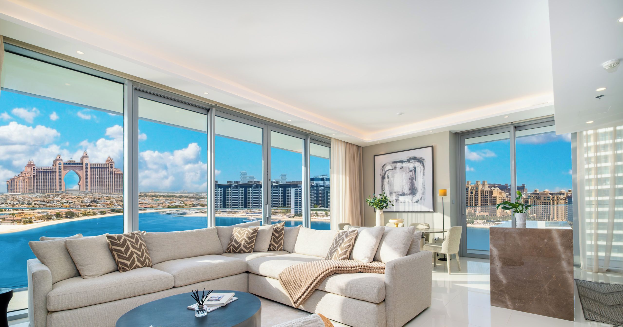 A modern living room with a large sectional sofa, a coffee table, and a view of the city and water.