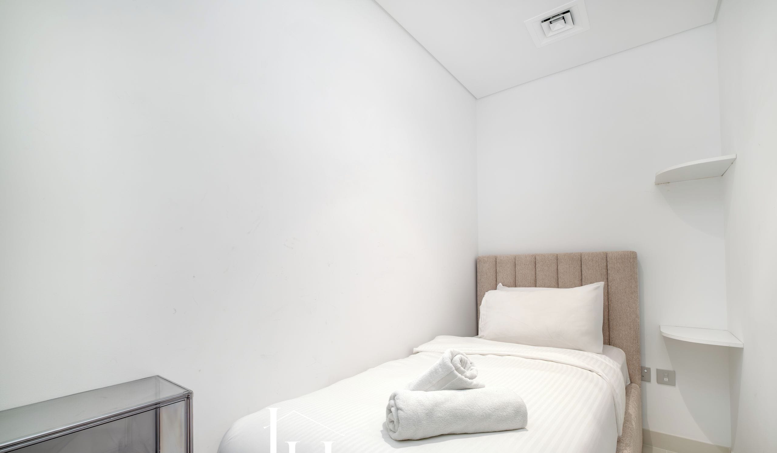 Una habitación de hotel moderna y minimalista con una cama bien hecha, una mesita de noche y un estante empotrado.