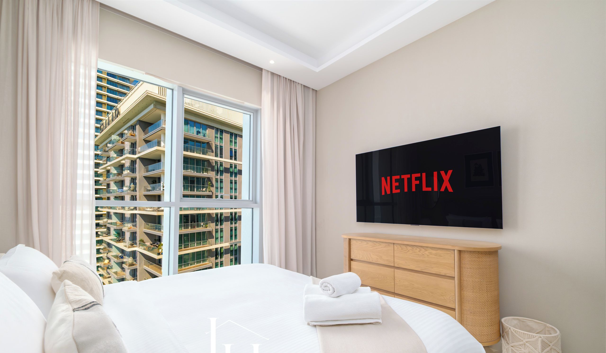 A hotel room with a large bed, a TV mounted on the wall, and a view of high-rise buildings.