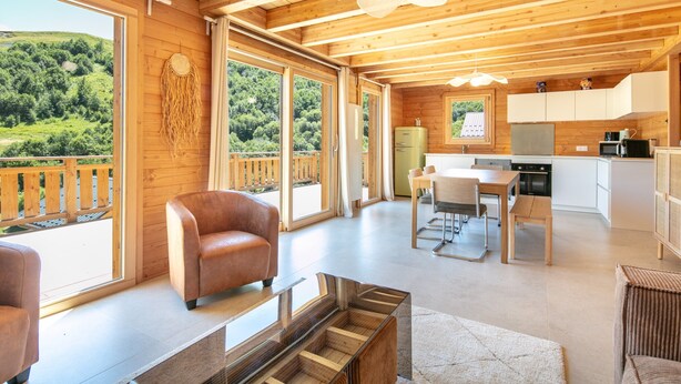A modern wooden cabin with a kitchen, dining area, and a large window overlooking a forested area.