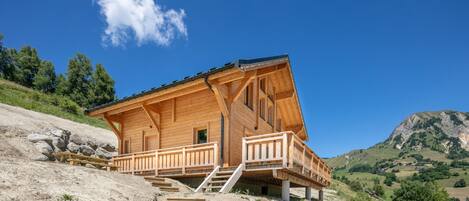 Une cabane en bois dotée d’un balcon, située sur une colline et offrant une vue dégagée sur le paysage environnant.