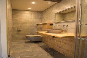 Ein modernes Badezimmer mit Duschkabine aus Steinplatten, einem Holzkosmetikschrank mit Waschbecken und einer Toilette.