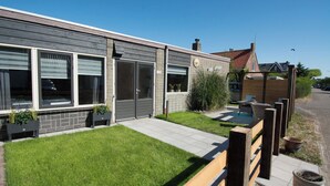 A modern house with a well-maintained lawn, a wooden deck, and a small outdoor seating area.