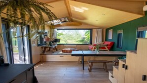 Een moderne keuken met houten kastjes, een eettafel en een groot raam met uitzicht op de natuur.
