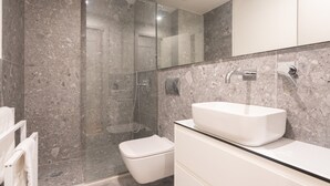 A modern bathroom with a glass-enclosed shower, a white toilet, and a large white sink. - LIV Athinum 1 - Luxury Apartment 4C (Athens)