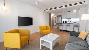 A modern living room with a sofa, two yellow armchairs, a white coffee table, and a flat-screen TV mounted on the wall. - LIV Athinum 1 - Luxury Apartment 4C (Athens)