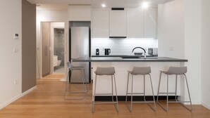 A modern kitchen with a central island, bar stools, and a view into the adjacent bathroom. - LIV Athinum 1 - Luxury Apartment 4C (Athens)