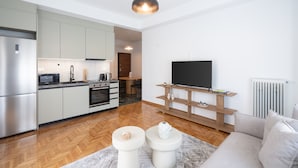 Cozinha moderna com micro-ondas, forno e pia, área de jantar com mesa e cadeiras, e sala de estar com sofá e televisão.