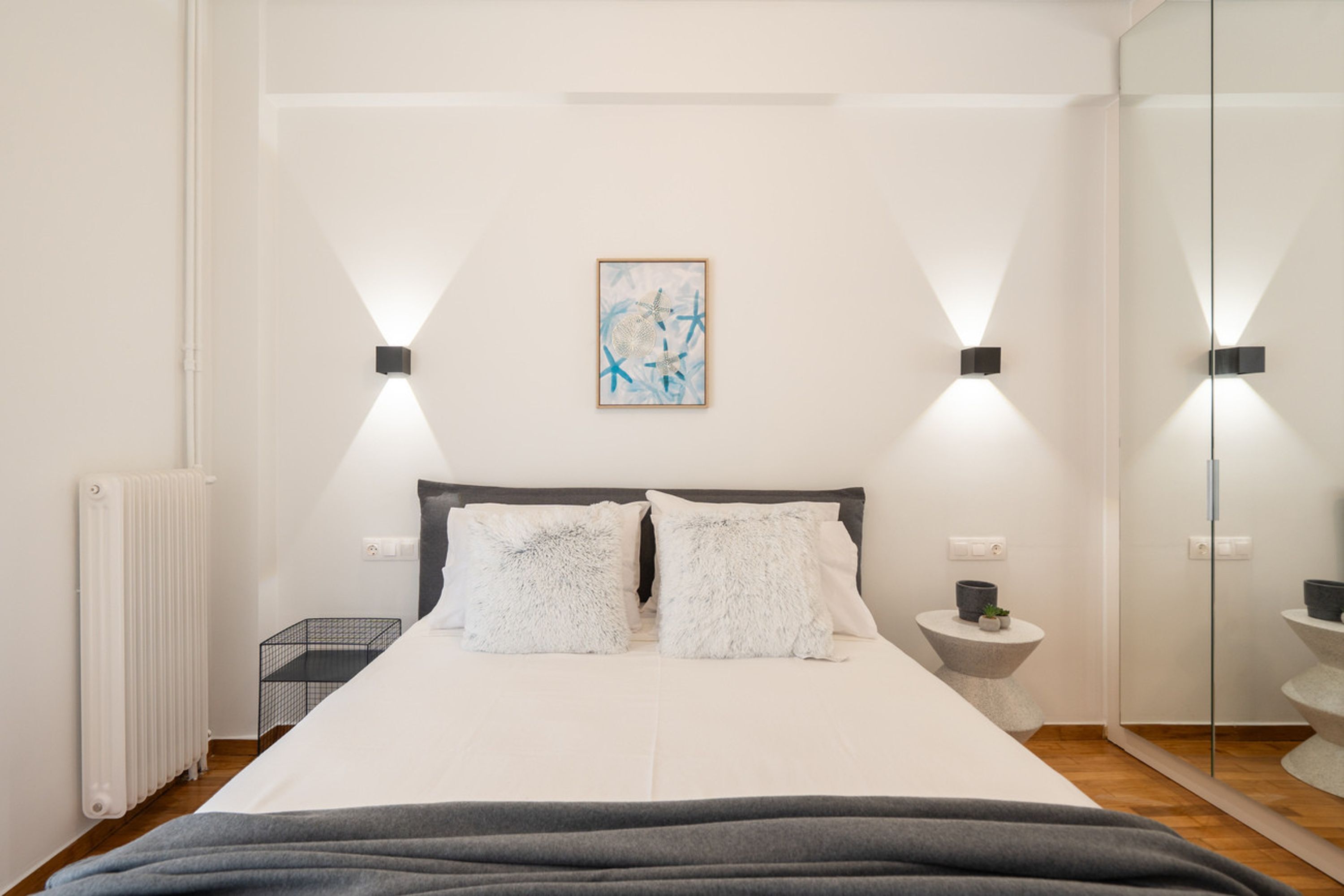 A modern bedroom with a large bed, bedside tables, a wall-mounted artwork, and a mirror.