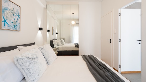 Quarto moderno com cama grande, mesa de cabeceira, espelho e porta.
