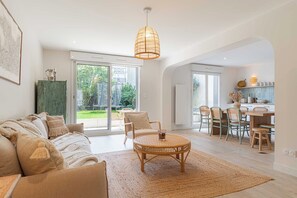 A spacious living area with a rattan coffee table, a sofa with cushions, and a dining area with chairs and a table.