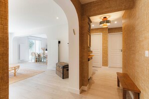 A spacious interior with an arched doorway, a dining area with chairs, a bench, and a suitcase.