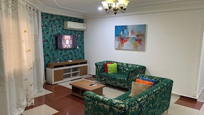 Una sala de estar con un sofá verde, un televisor y un cuadro en la pared.