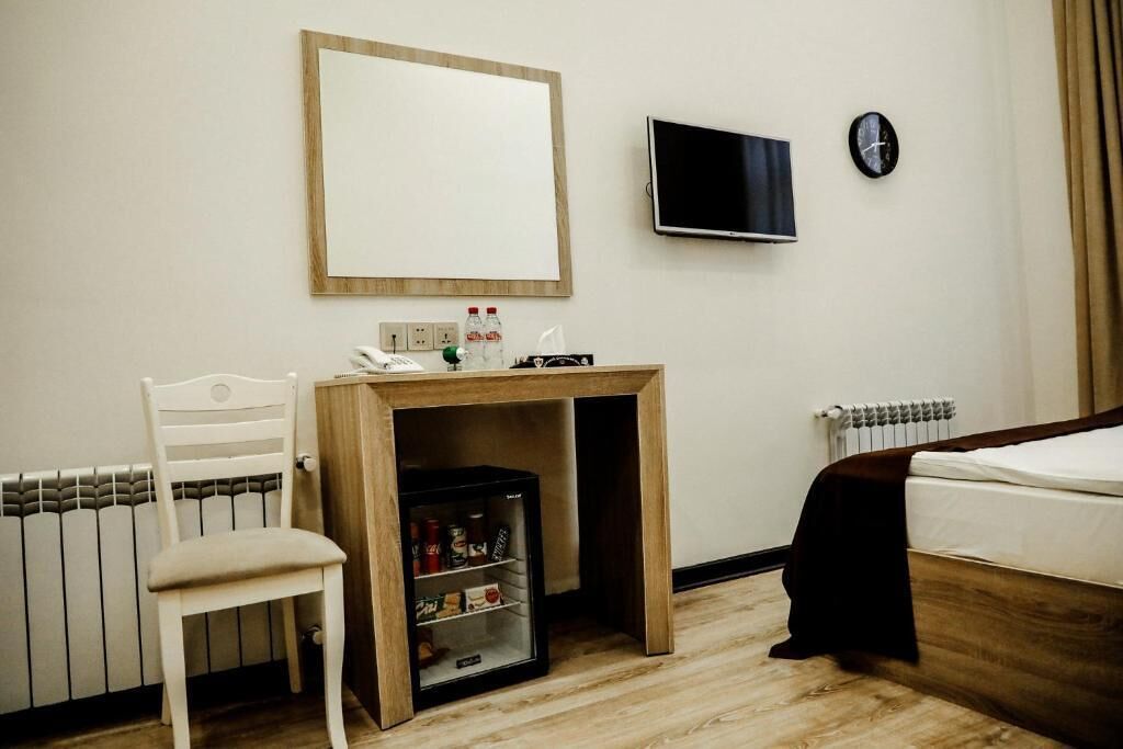 Ein Hotelzimmer mit einem Bett, einem Schreibtisch mit Spiegel, einem Fernseher, einer Uhr und einer Heizung.